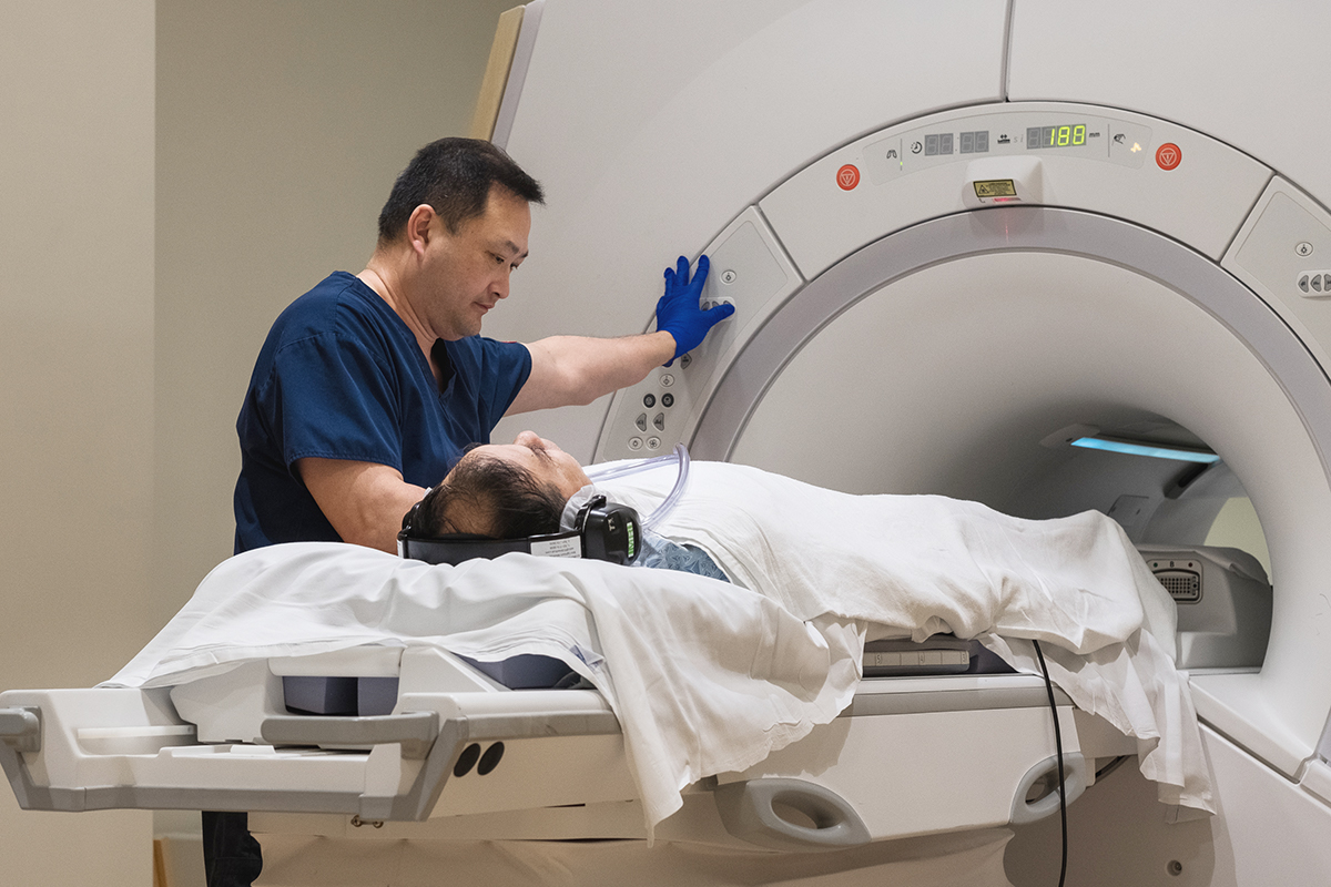 a radiology technician is operating MRI machine. a patient is lying on the bed