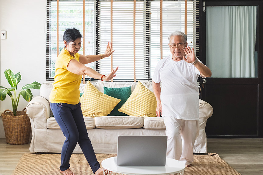 a female and a male are doing taichi at home looking at a laptop