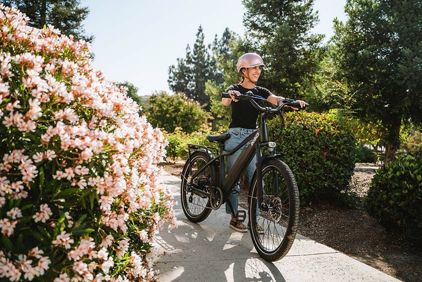 一個女人推著單車在開滿花的人行道上笑著走
