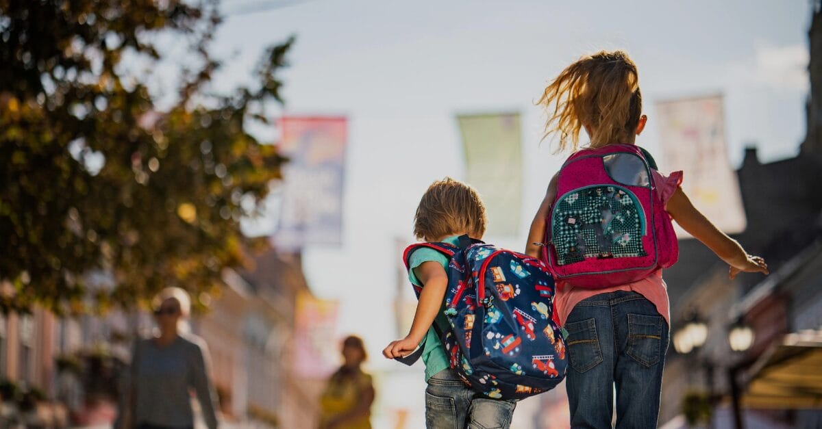 two kids wearing backpacks walking on the streets