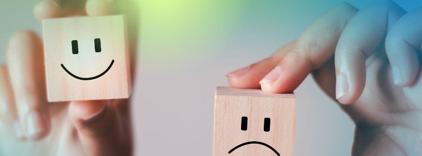 a hand holding a wooden block with a sad face